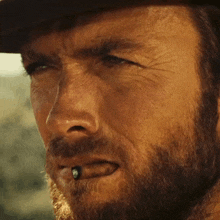 a close up of a man 's face with a cowboy hat and a cigarette in his mouth