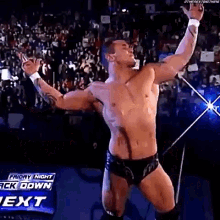 a shirtless wrestler is standing in a ring with his arms outstretched .