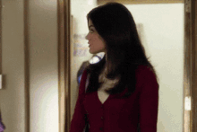 a woman in a red cardigan is standing in a doorway looking at something .