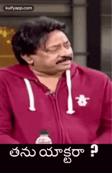 a man in a red hoodie is talking in telugu .