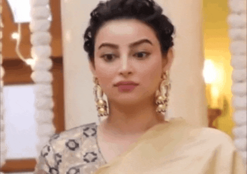 a woman wearing a saree and earrings is standing in front of a wall .