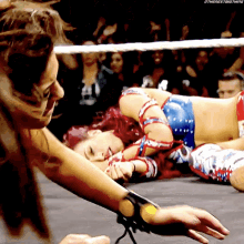 a female wrestler is laying on the ground while another wrestler holds her arm up