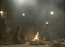 a man and a woman sit around a fire in a dark room