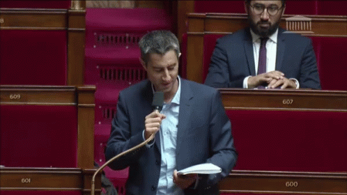 a man in a suit is speaking into a microphone in front of a row of empty seats with the number 607 on them