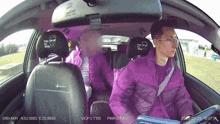 a man in a purple jacket is driving a car with a sticker on the back seat that says pw-otaxi