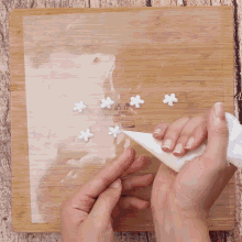 a person is piping white flowers on a wooden cutting board with a sticker that says ' a ' on it
