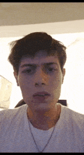 a young man wearing a white t-shirt and a chain around his neck is making a funny face