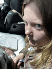 a woman sits in a car with a notebook and a pen in her hand