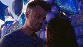 a man and a woman are kissing in front of a bunch of balloons .