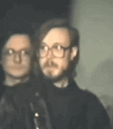 a man with glasses and a beard is standing next to another man with glasses .