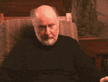 a man with a beard is sitting in a chair and looking at the camera