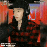a man wearing headphones and a plaid shirt is standing in front of a t98 strong sign