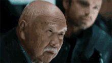 an elderly man with a mustache is making a funny face while sitting next to another man .