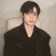 a young man in a black jacket is sitting in a chair and making a funny face .