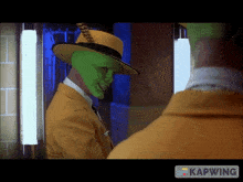 a man wearing a green mask and a yellow hat is looking at himself in a mirror