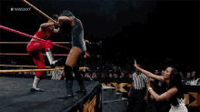 two women are wrestling in a wrestling ring while a referee looks on .