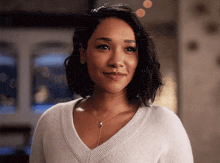 a woman wearing a white sweater and a necklace is smiling and looking at the camera .