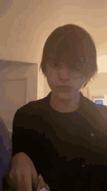 a young man in a black shirt looks at the camera with a serious look on his face