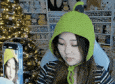 a woman wearing a green hat is taking a picture of herself with her phone