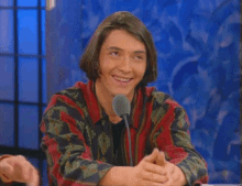 a young man is smiling in front of a microphone while sitting at a table