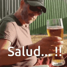 a man is sitting at a table holding a glass of beer with the word salud written on it .