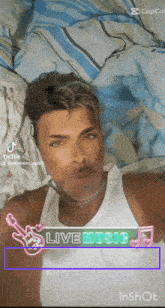 a man in a white tank top is laying on a bed with a live music banner behind him .
