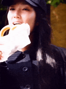 a woman wearing a black hat and a black coat eating a donut