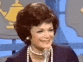 a woman wearing a pearl necklace and earrings is smiling into a microphone .
