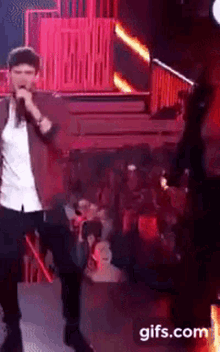 a man singing into a microphone on a stage with a gifs.com watermark on the bottom