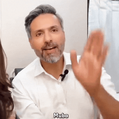 a man with a beard wearing a white shirt and a microphone is talking to a woman and says 
