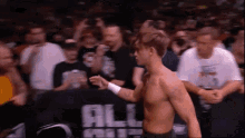 a shirtless man stands in front of a banner that says all