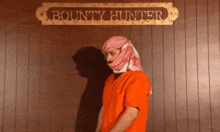 a man in a prison uniform stands in front of a sign that says bounty hunter