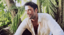 a man in a white shirt is sitting under a tree .