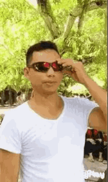 a man wearing sunglasses and a white shirt is adjusting his sunglasses .