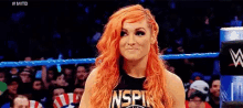 a woman with red hair is standing in a wrestling ring looking at the camera .