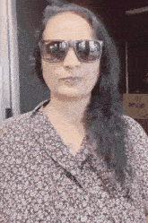 a woman wearing sunglasses and a floral shirt has a box in the background
