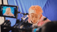 a young man with pink hair is sitting in front of a camera .