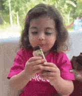 a little girl in a pink shirt is eating a chocolate bar