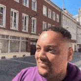 a man wearing a purple sweatshirt stands in front of a brick building