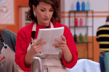 a woman in an apron is reading a piece of paper with rtve written on the bottom right