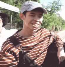 a young man wearing a striped shirt and a hat smiles