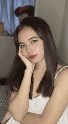 a woman in a white tank top with her hand on her chin