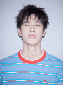 a young man wearing a blue and red striped shirt winks