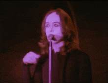 a man singing into a microphone with a purple light behind him