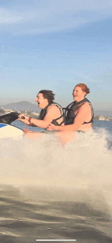 two women in bikinis are riding a jet ski