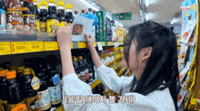 a woman is reaching for a bottle of soy sauce in a grocery store