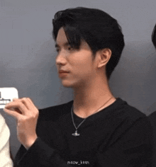 a young man wearing a black sweater and a necklace is holding a cell phone .