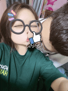 a woman wearing glasses is kissing a man who is wearing a green shirt that says hot tech