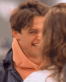 a man in a pink hoodie is laughing with a woman in a white shirt