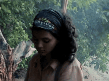a woman wearing a survivor headband stands in the woods
